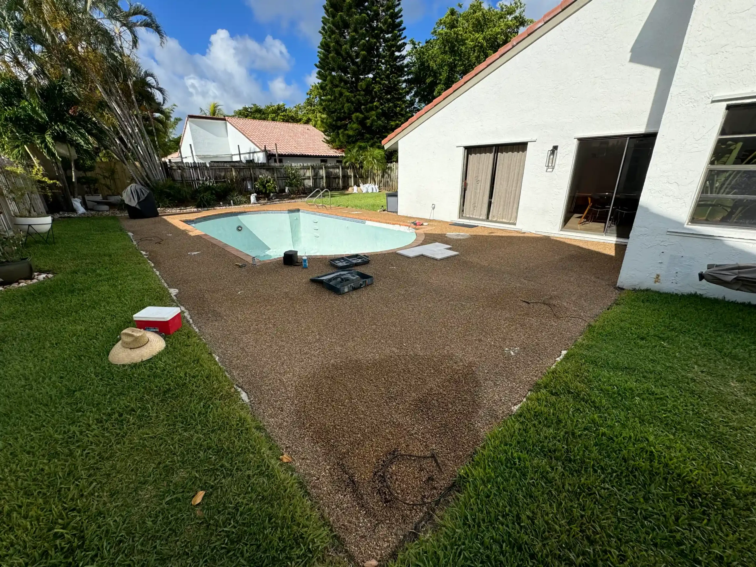 In-progress paver installation for a residential pool deck in Fort Lauderdale, South Florida. Showing brown/earth-toned pavers near white house.