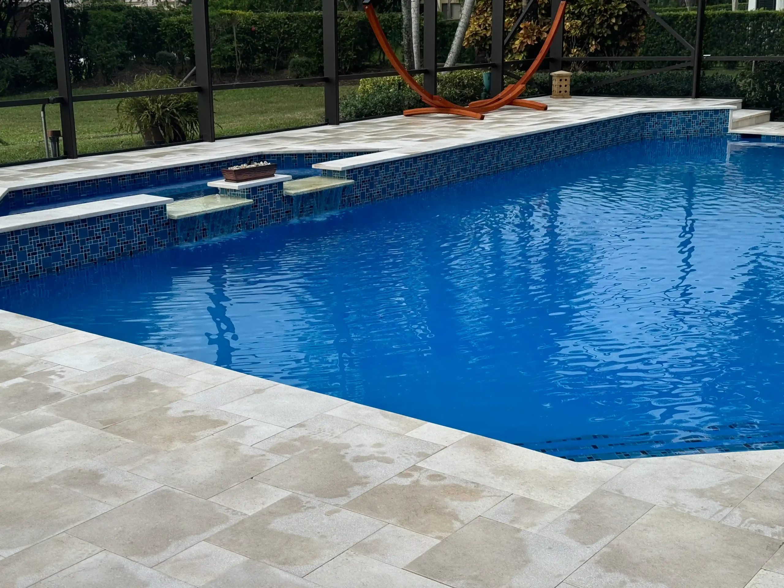 Completed luxury pool deck featuring large format Travertine pavers and modern outdoor furniture overlooking the water in Miami Beach.