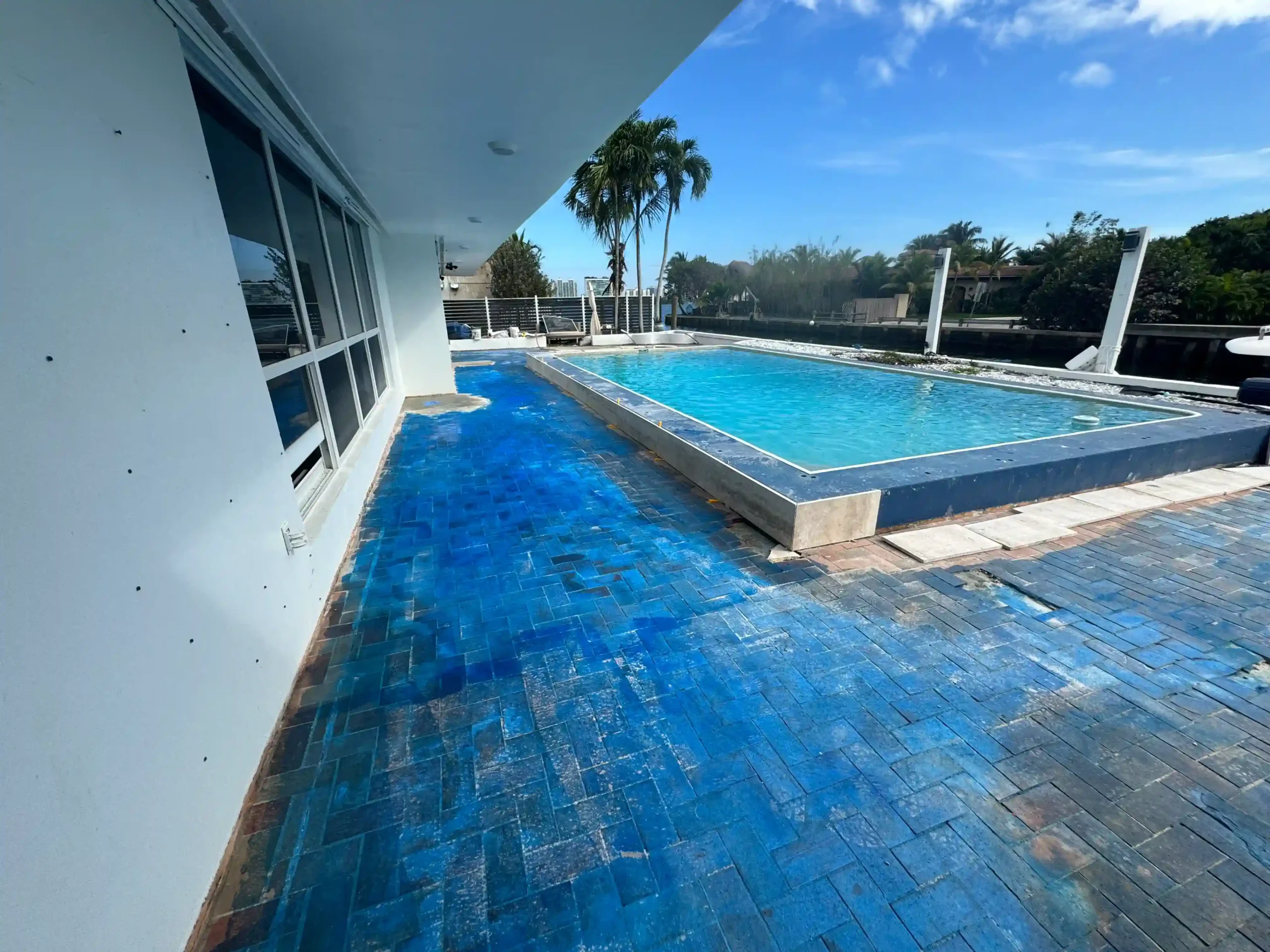 Before: Deteriorated blue-painted brick pavers on a residential pool deck in Miami, FL. Pavers require immediate removal and replacement with Travertine.