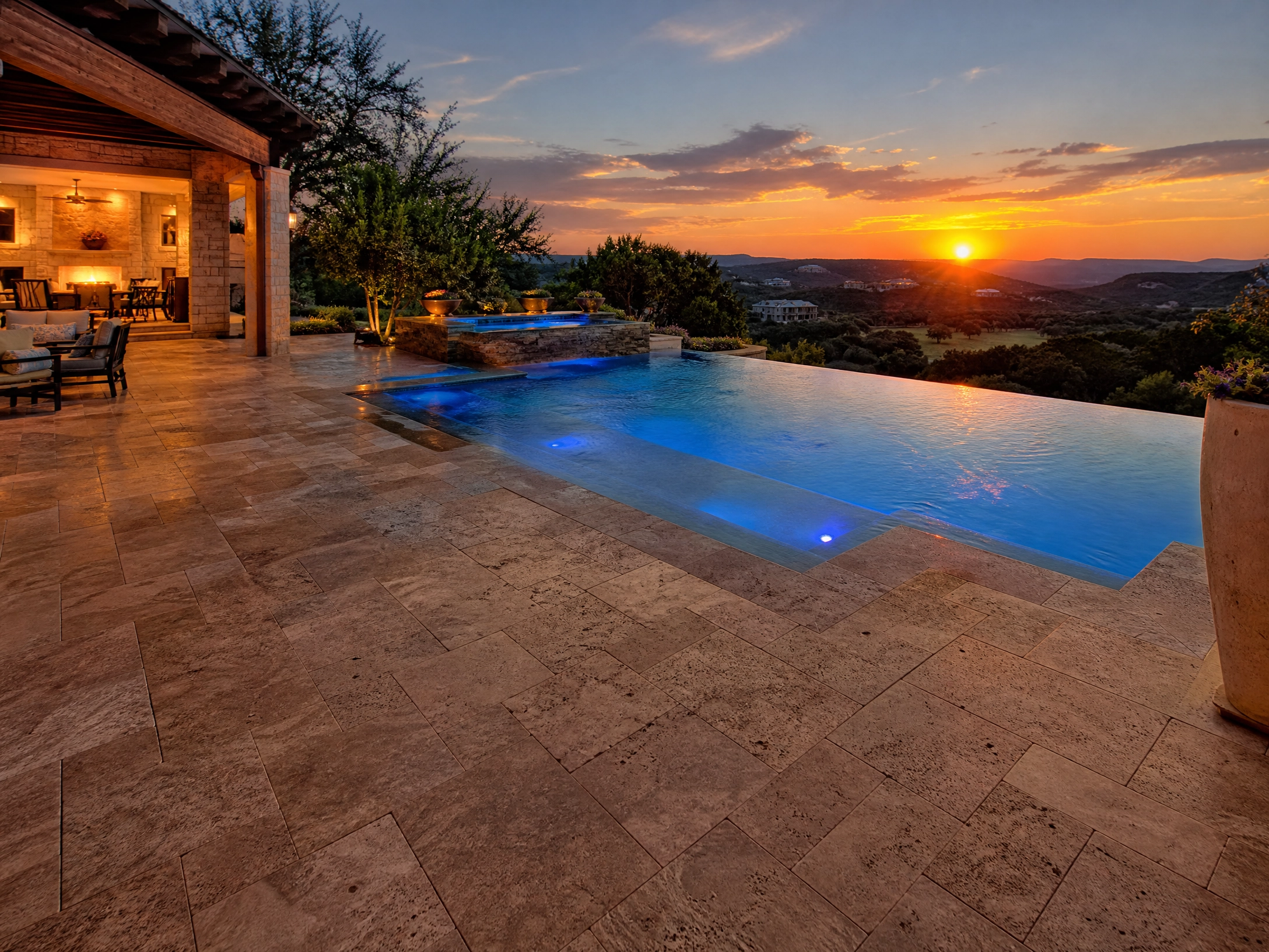 Luxury pool with travertine pavers and scenic sunset view.