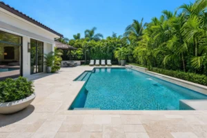 Beautiful backyard pool with travertine pavers and lush greenery.